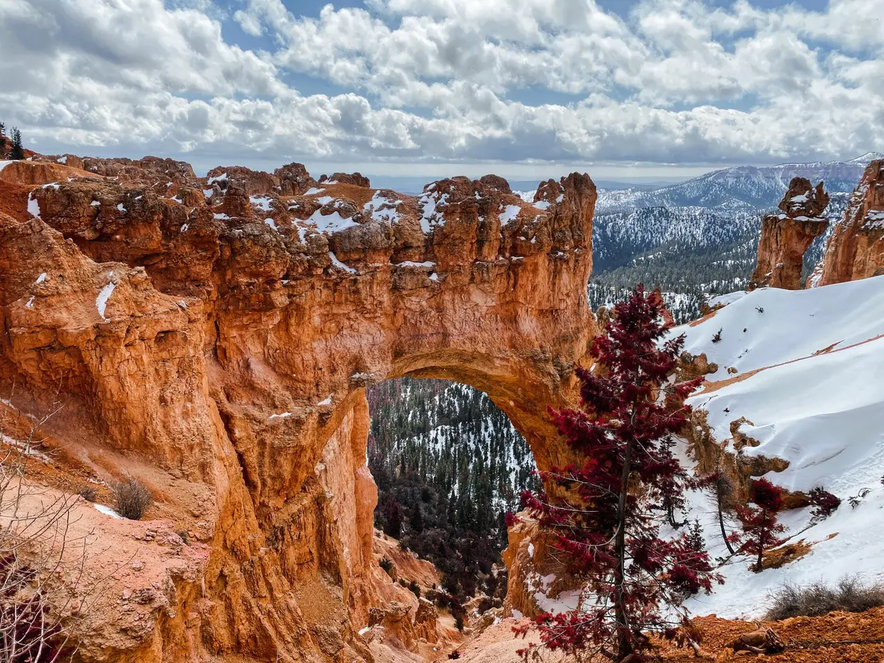 A red-rock arch and snow-dusted canyon beneath a cloudy sky